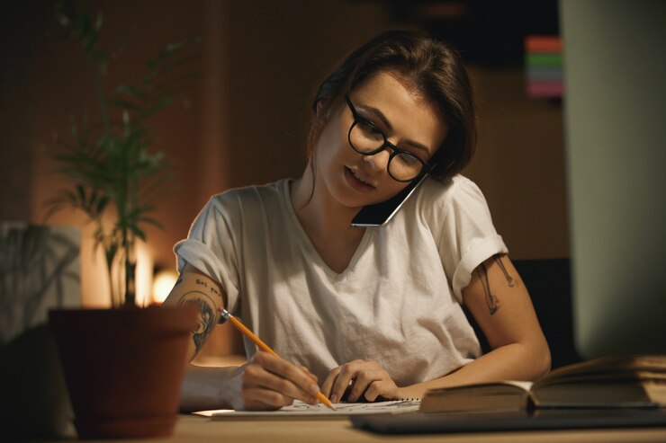 Woman writing on a notebook while talking on the phone